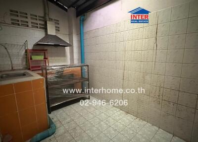 A small kitchen with tiled walls and floor, featuring a sink, stove, and storage spaces.