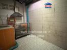 A small kitchen with tiled walls and floor, featuring a sink, stove, and storage spaces.