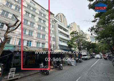 Street view of a multi-storey residential building with parked motorbikes and vehicles