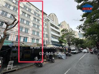 Street view of a multi-storey residential building with parked motorbikes and vehicles