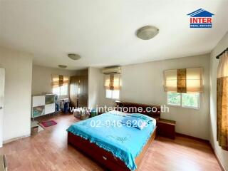 Spacious bedroom with a wooden floor, large windows, and a bed with blue bedding.