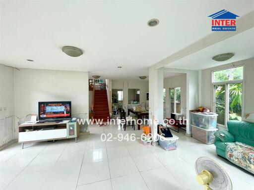 Spacious living room with white tiled flooring, a TV, and a green couch