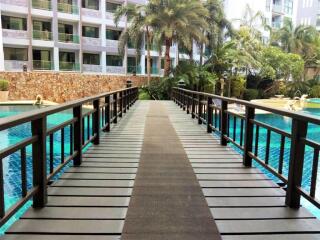 Walkway over swimming pool with palm trees and building in the background