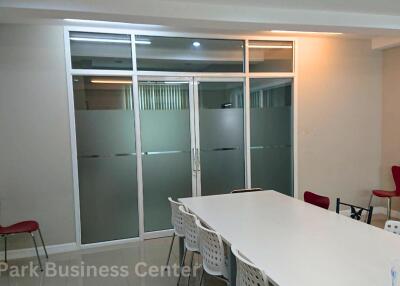 Meeting room with glass partitions, white table, and red chairs