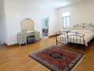 Spacious bedroom with hardwood floor, iron bed frame, and a vintage dresser