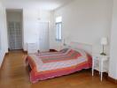 A spacious bedroom with a colorful bedspread and wooden flooring.