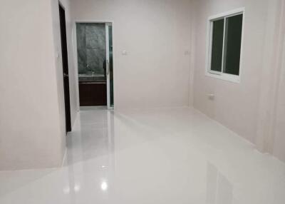 Empty room with glossy white tiles, window, and door leading to a bathroom