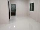 Empty room with glossy white tiles, window, and door leading to a bathroom