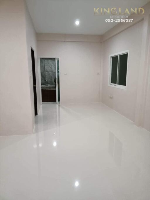 Empty room with glossy white tiles, window, and door leading to a bathroom