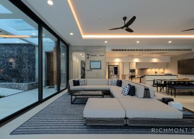 Modern living room with large windows, sectional sofa, and open concept kitchen