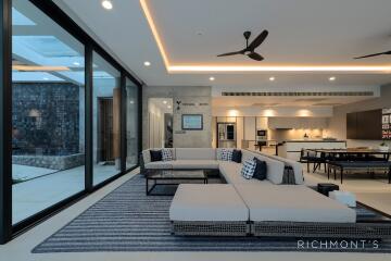 Modern living room with large windows, sectional sofa, and open concept kitchen