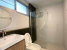 Modern bathroom with round mirror, sink, toilet, and glass shower area