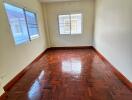 Empty bedroom with wooden floor and two windows