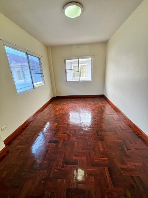 Empty bedroom with wooden floor and two windows