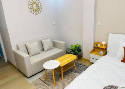 Minimalist bedroom with white bed, small beige couch, wooden side table, and plants