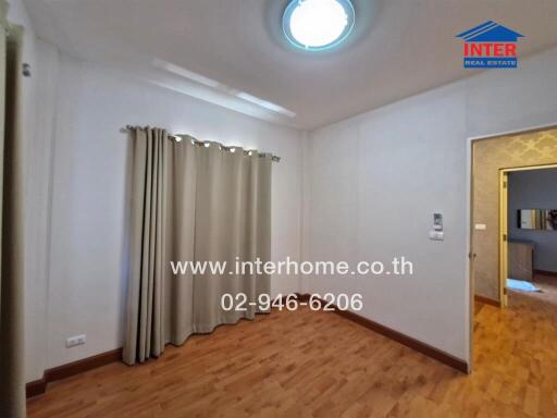 Bedroom with wood flooring, curtained window, and view of another room