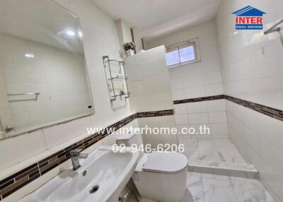 Modern bathroom with tiled floor, sink, toilet, shower area, and a small window.