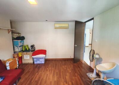 A cluttered bedroom with wooden flooring, storage boxes and an air conditioner