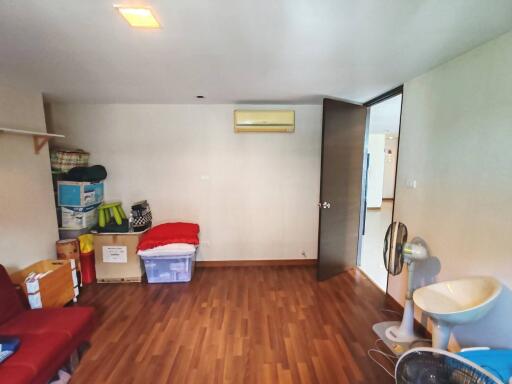 A cluttered bedroom with wooden flooring, storage boxes and an air conditioner