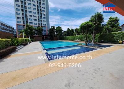 Outdoor swimming pool area with a large pool, surrounding trees, and adjacent building