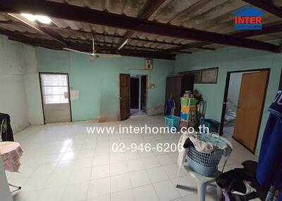 A room with a tiled floor, open ceiling, and several doors, featuring laundry baskets, storage bins, and hanging clothes.