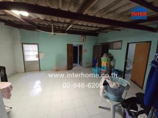 A room with a tiled floor, open ceiling, and several doors, featuring laundry baskets, storage bins, and hanging clothes.