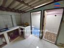 Small kitchen area with tiled backsplash and sink, adjacent to bathroom