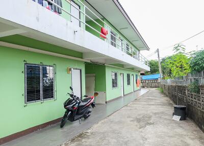 Two-story green building with a long walkway and a parked motorcycle