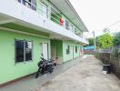 Two-story green building with a long walkway and a parked motorcycle