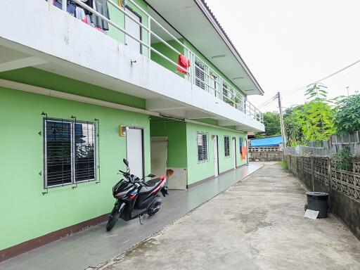 Two-story green building with a long walkway and a parked motorcycle