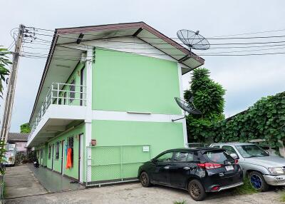 Two-story green building with parked cars and satellite dish