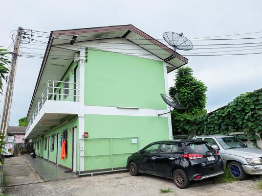 Two-story green building with parked cars and satellite dish