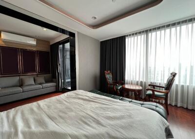 Spacious bedroom with a large window, cozy bed, seating area, and modern decor