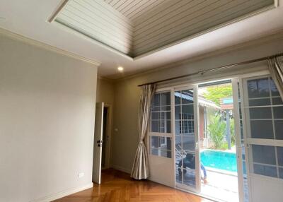 Empty living room with wooden floor, large windows, and view of a swimming pool outside