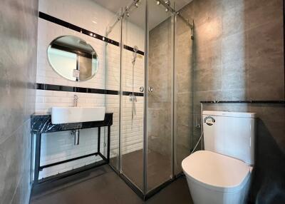 Modern bathroom with glass shower enclosure, round mirror, and white sink