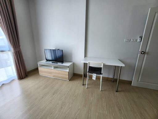 Living room with wooden flooring, a small TV stand with a flat screen TV, and a small desk with a chair