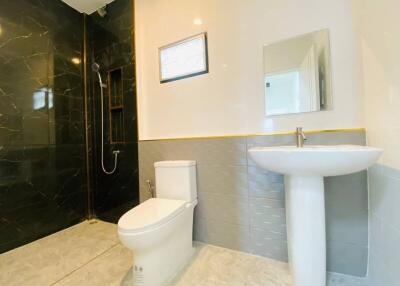 Modern bathroom with black tile shower area, white toilet, and white pedestal sink.