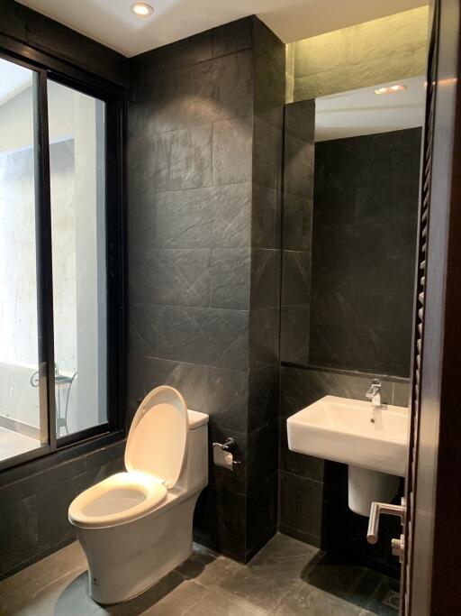 Modern bathroom with dark tiles, toilet, and sink