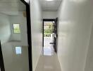 Bright hallway with white walls and polished floor, leading to a room and a balcony