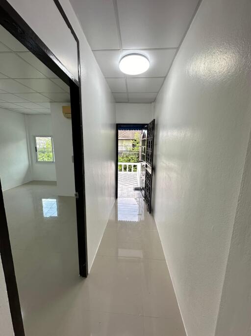 Bright hallway with white walls and polished floor, leading to a room and a balcony