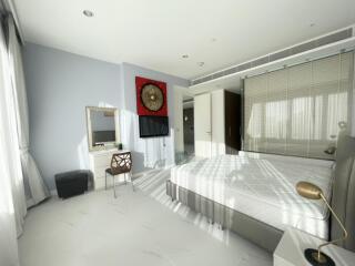 Modern bedroom with double bed, dressing table, wall art, and ample lighting.