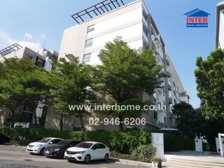 Modern apartment building exterior with cars parked and lush greenery