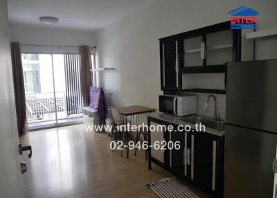 A modern kitchen with black cabinets and stainless steel appliances, attached to a living area with a balcony.