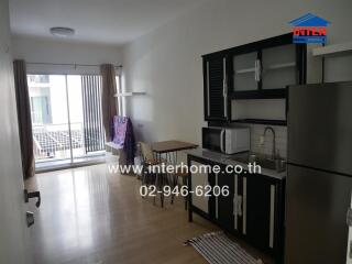 A modern kitchen with black cabinets and stainless steel appliances, attached to a living area with a balcony.