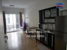 A modern kitchen with black cabinets and stainless steel appliances, attached to a living area with a balcony.