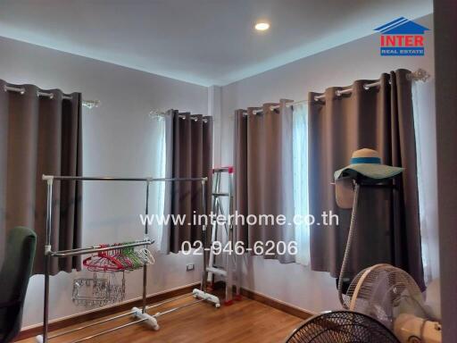 A bedroom with windows, curtains, and clothes drying racks.