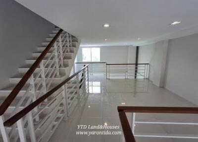 Staircase with railing in an open area of a building with tiles and large windows.