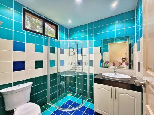 Modern bathroom with blue-green tile design, glass shower enclosure, and vanity