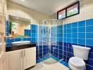 Modern bathroom with blue and white tiles, a sink, a shower, a toilet, and a window