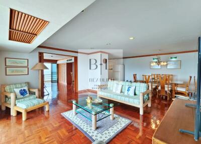 Spacious living room with wooden flooring, couch, armchair, coffee table, and dining area